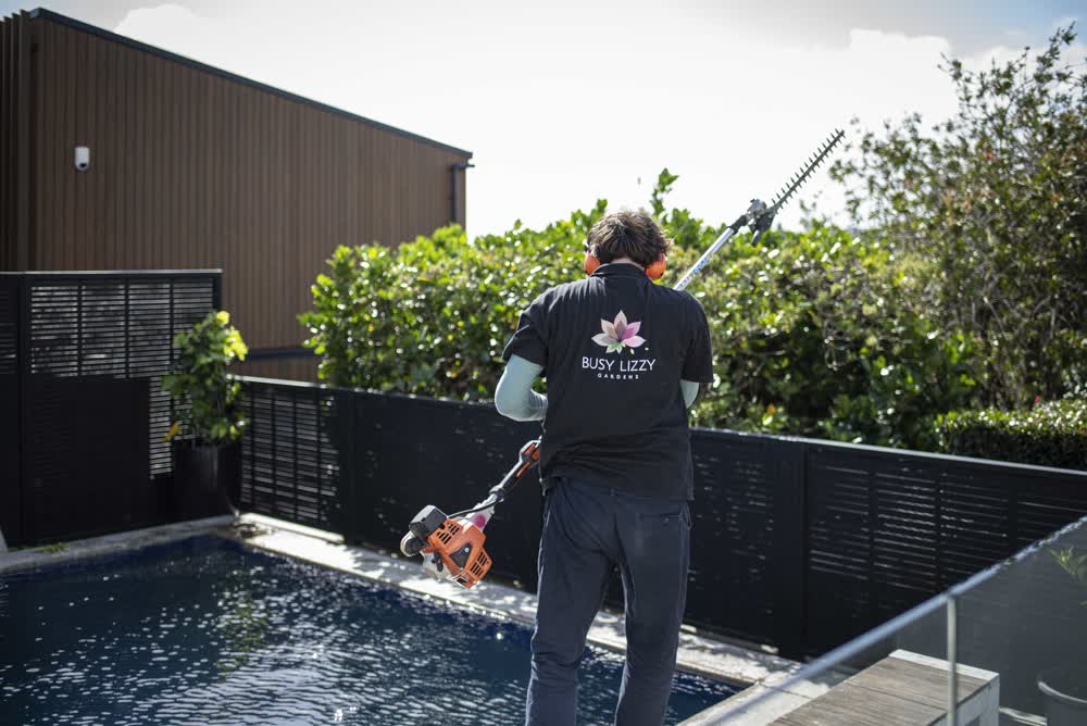 Man trimming hedge near pool area